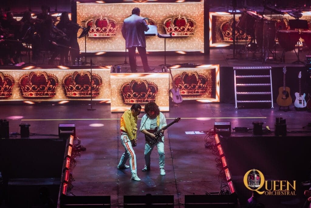 Shot of our Freddie and Brian of QUEEN Orchestral at the 3Arena, stage bathed in gold light, the Queen crown and the crowd were on their feet.